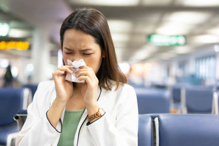 Woman sneezing in tissue while waiting for train at the airport