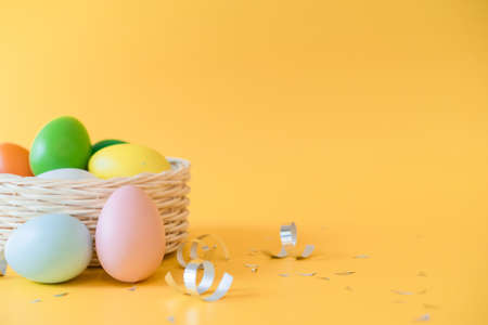 Colorful Easter eggs in a basket and serpentine on a yellow background