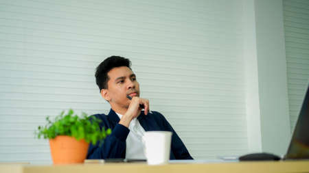 Portrait of Asian businessman sitting at his desk in office and thinking.