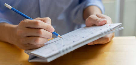 close up on employee man hand using pen to writing schedule on calendar to make appointment meeting or manage timetable each day at house for work from home conceptの写真素材