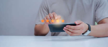close up on customer man hand pressing on smartphone screen with gold five star rating feedback icon...