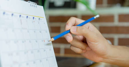 close up on employee man hand using pen to writing schedule on calendar to make appointment meeting or manage timetable each day at house for work from home conceptの写真素材