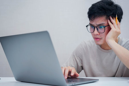 close up young asian man stress with working job at laptop desk at home in quarantine and major of depressive disorder conceptの写真素材