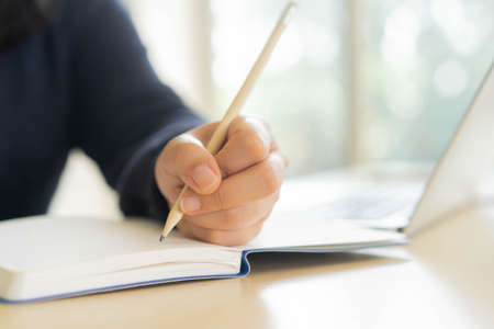 close up woman hand using pencil to writing homework or practice exam before test while opening...