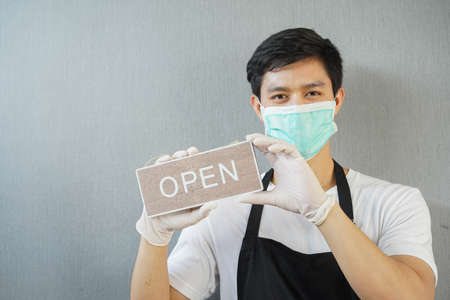 close up young business owner man holding open sign board to promote and inform reopening after lock...