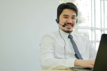 close up asian man call center agent wear headset device and smiling working in operation room with service-mind at desktop table , telemarketing and help desk conceptの写真素材
