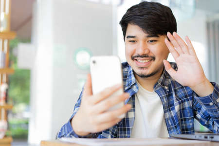 close up young middle eastern man sitting at the park and using video call form smartphone to talking with friends and family for new normal and healthy lifestyle conceptの写真素材
