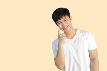 close up young asian man applying sunscreen uv-protection on face and smile while thinking and looking on grey background for advertising product conceptの写真素材