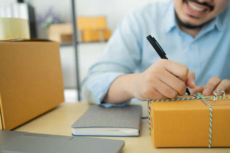 close up young businessman (owner) writing customer's address on the packing box after confirming...