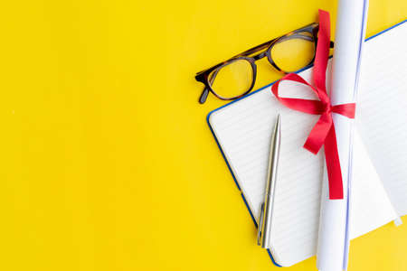 close up top view of certificated degree with notebook and pen and glasses on yellow background for education conceptの写真素材