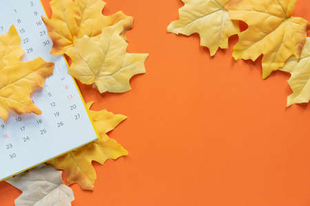 Autumn calendar with yellow leaves on orange background, top view. Space for textの写真素材