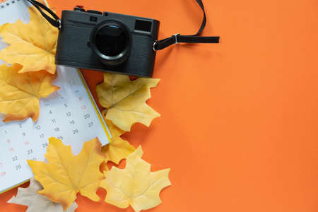 Calendar, camera and autumn leaves on orange background. Space for textの写真素材