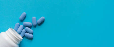 Blue pills spilling out of bottle on blue background, top view. Space for textの写真素材