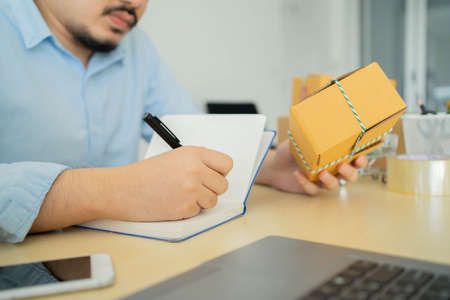 close up young business owner sitting at home office on the table while writing detail of customer's...