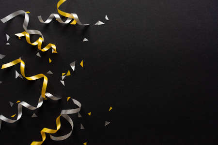 close up on group of silver and gold color of rolling ribbon and confetti on black background with...