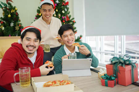 Group of Asian friends eating pizza and drinking beer while celebrating Christmas at homeの写真素材