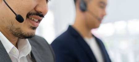 close up asian man call center agent wear headset device and smiling working in operation room with service-mind at desktop table , telemarketing and help desk conceptの写真素材