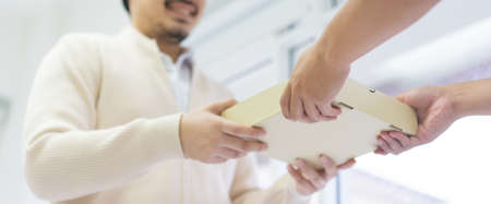 Close-up of a young man receiving a parcel from a delivery man
