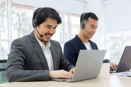 close up asian man call center agent wear headset device and smiling working in operation room with...