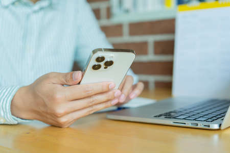 Close-up of a man using a smart phone while sitting at a wooden table.