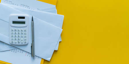 close up top view on calculator and open over group of invoice letter mail from bank on yellow background for money and debt management conceptの写真素材