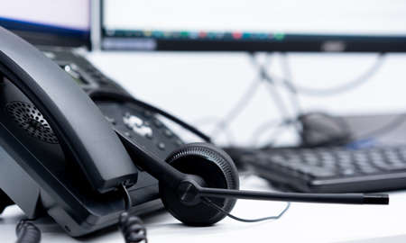 Close-up of telephone receiver and headset on desk in call centerの写真素材