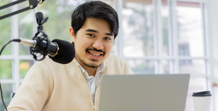 Young asian male radio host using a microphone and laptop to record a podcast or online show.の写真素材