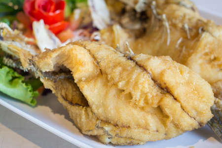 Deep fried snapper with fish sauce in white dish on stone table.の写真素材