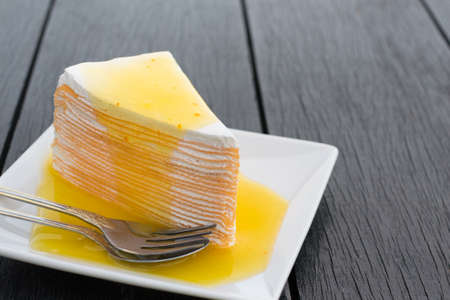 Orange crepe cake in white dish on black wooden table.の写真素材