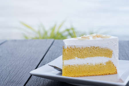 Cream butter cake in white dish on wooden table with sea background.の写真素材