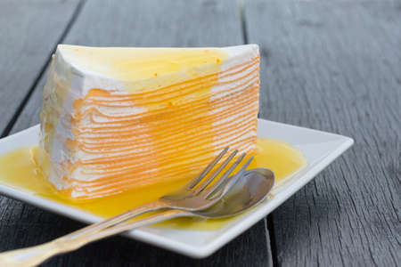 Orange crepe cake in white dish on black wooden table.の写真素材