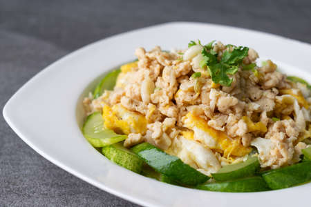 Fried cucumber with chicken egg in white dish on concrete table.の写真素材