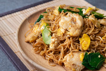 Fried dry instant noodle with chicken and chinese kale in wooden dish on concrete table.の写真素材