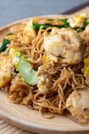 Fried dry instant noodle with chicken and chinese kale in wooden dish on concrete table.の写真素材