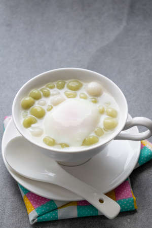 Pandan Thai glutinous rice balls (Bua Loi) in white bowl on table,Boiled egg.の写真素材