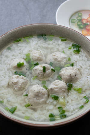 Rice soup with chicken ball and scallion in gray bowl on table.の写真素材