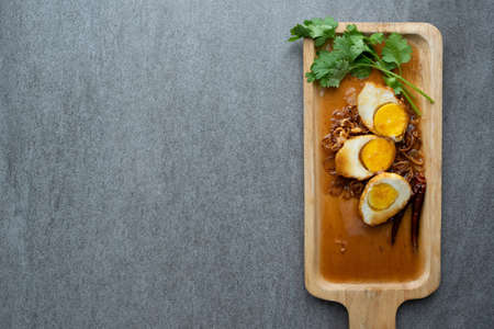 Boiled and Fried eggs in sweet and sour sauce with coriander in the wooden dish on table.