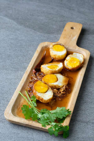 Boiled and Fried eggs in sweet and sour sauce with coriander in the wooden dish on table.