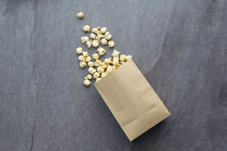 Popcorn in paper cup pouring on table.