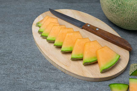 Melon sliced with pieces on wooden board on the concrete table.の写真素材