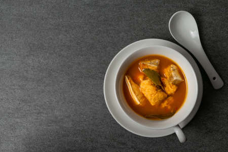 Spicy soup or orange curry of Thai with fish in white bowl and spoon on concrete table.の写真素材