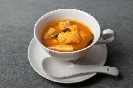 Spicy soup or orange curry of Thai with fish in white bowl and spoon on concrete table.の写真素材