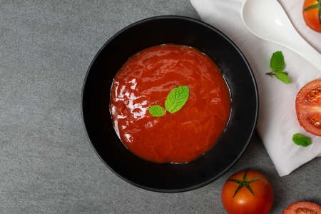 Tomato sauce and mint leaves in black bowl with tomatoes sliced on concrete table.