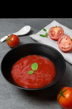 Tomato sauce and mint leaves in black bowl with tomatoes sliced on concrete table.の写真素材