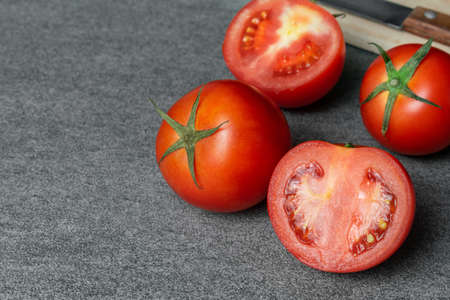 Group of haft tomatoes sliced with knife and wooden board on concrete table.の写真素材