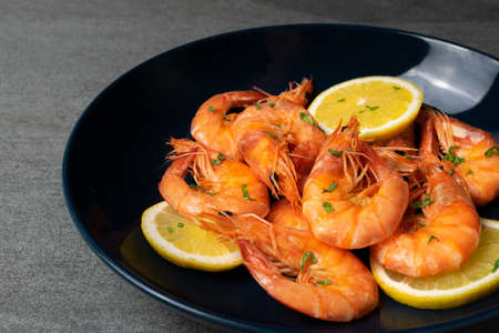 Boiled shrimp with lemon and parsley in blue plate on concrete table.の写真素材