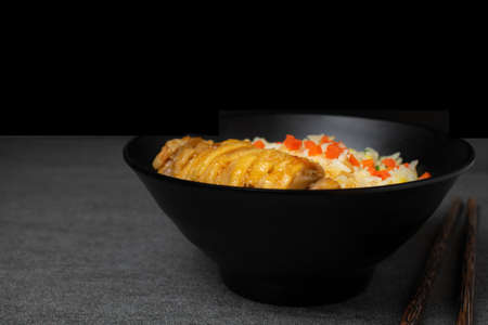Fried rice with roast chicken and carrot in Korean style in black bowl on table.の写真素材