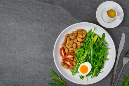 Arugula salad with almonds and tomato,boiled egg in white dish on tile table.の写真素材