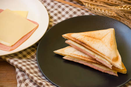 Sandwich stuffed with ham and cheese in black dish on wooden table.の写真素材