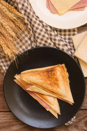 Sandwich stuffed with ham and cheese in black dish on wooden table.の写真素材